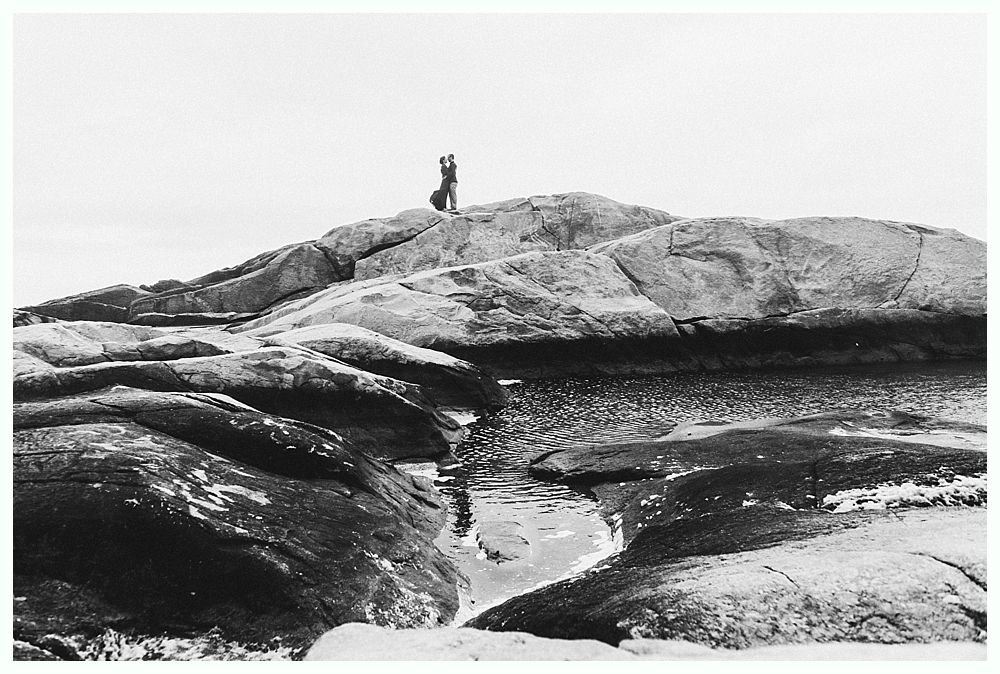 Person standing on a rocky outcrop overlooking a small pool of water.