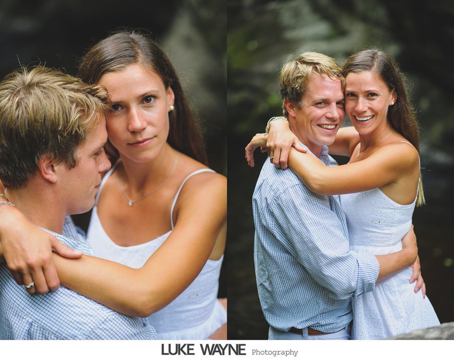 Couple embracing outdoors; woman in white dress, man in blue shirt, waterfall backdrop.
