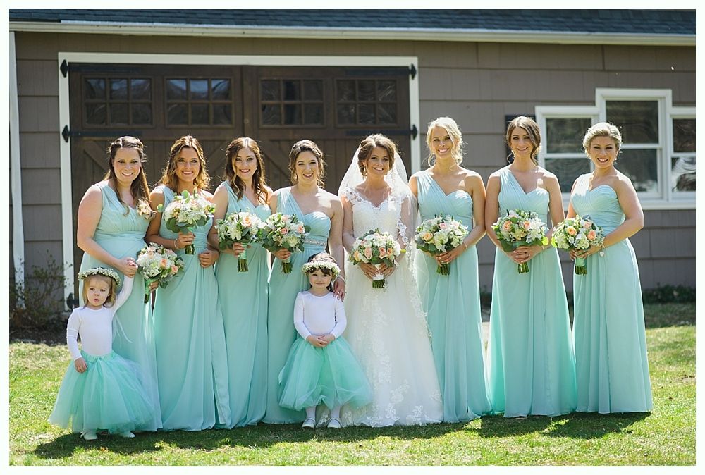 Bride and bridesmaids in teal dresses with bouquets pose in front of a building.