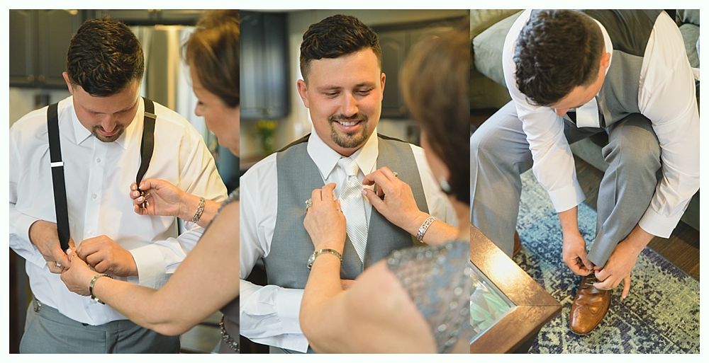 Man in a white shirt and gray vest being helped to get ready. Someone adjusts his suspenders, tie, and shoes.