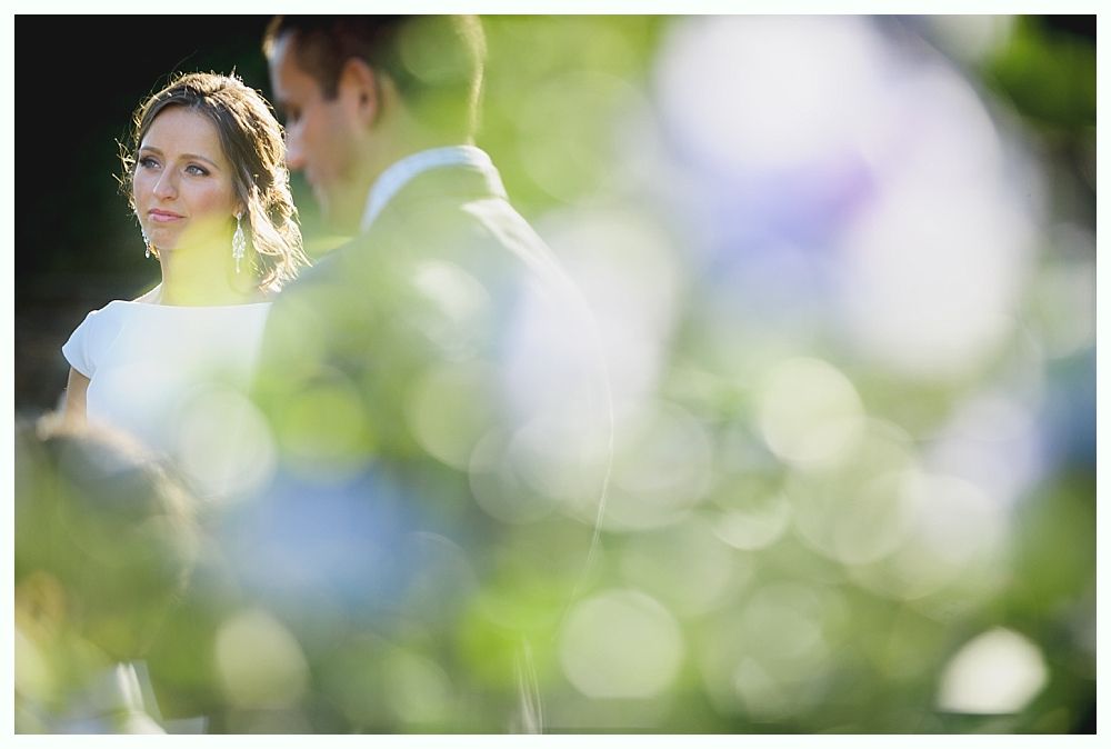 Bride with arms up, making a funny face, groom looking at his hand, cake cutting in background.