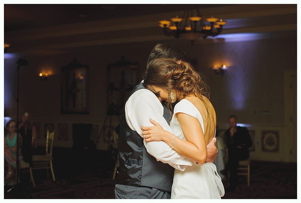 Bride with arms up, making a funny face, groom looking at his hand, cake cutting in background.