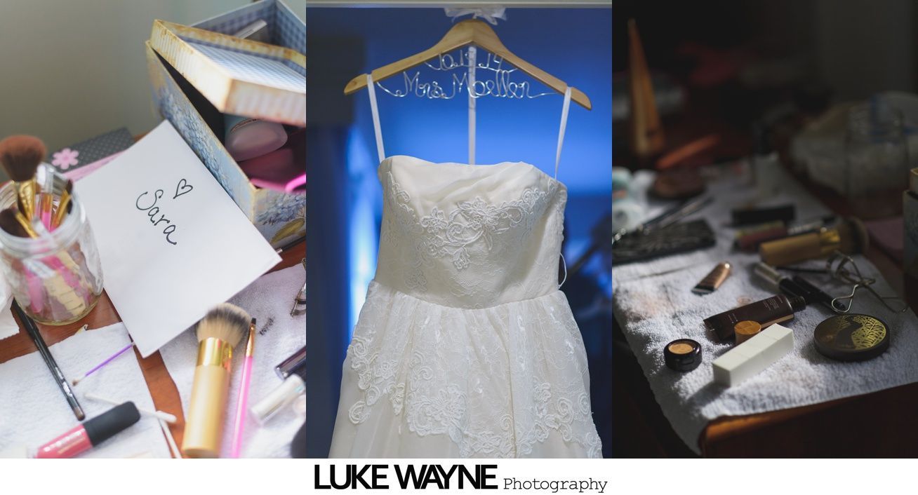 Wedding dress hanging, makeup supplies on table.