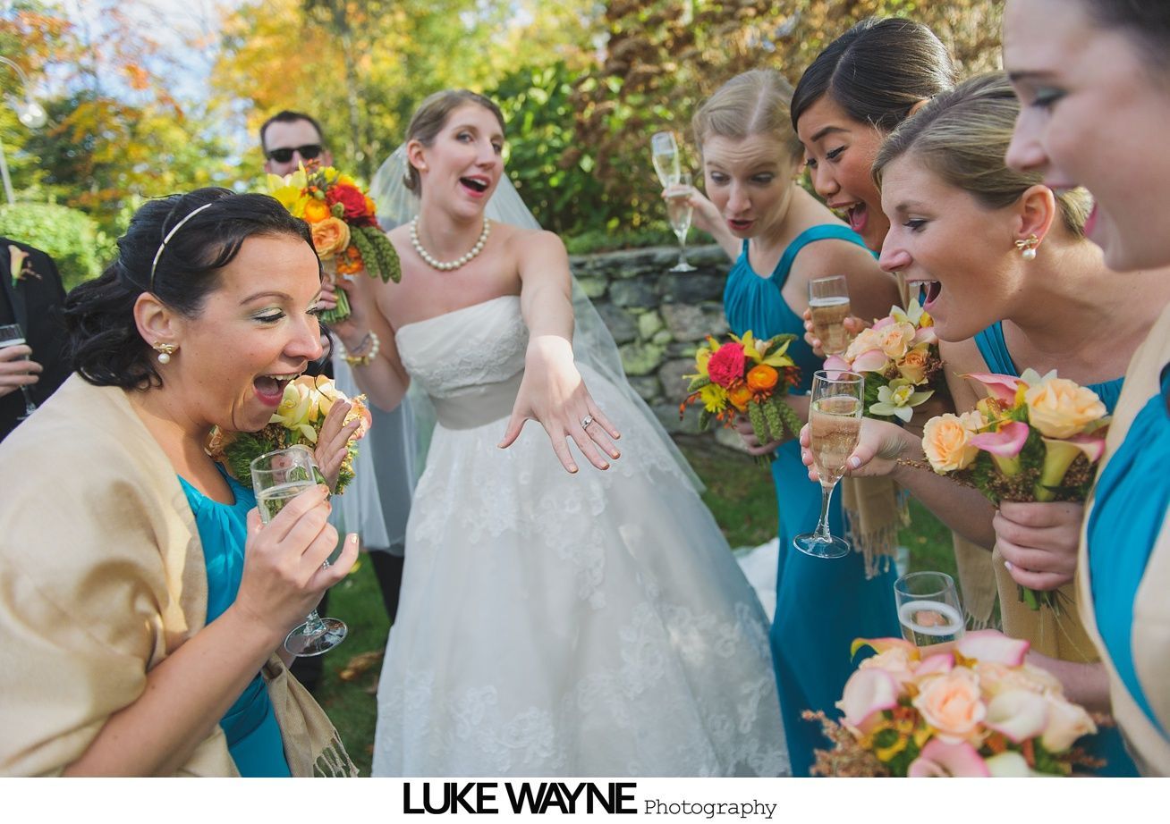 Bride showing ring, bridesmaids with champagne, bouquets; outdoor garden setting.