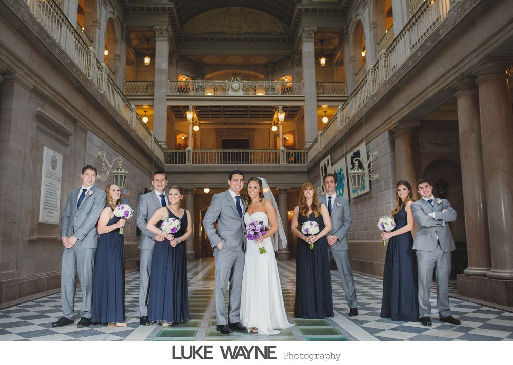 Wedding party posing in bar: bride on bar, groomsmen sprawled on floor, expressions of exhaustion.