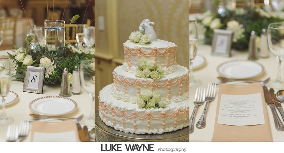 Three-tiered wedding cake with decorations, flanked by table settings with floral centerpieces and a table number.