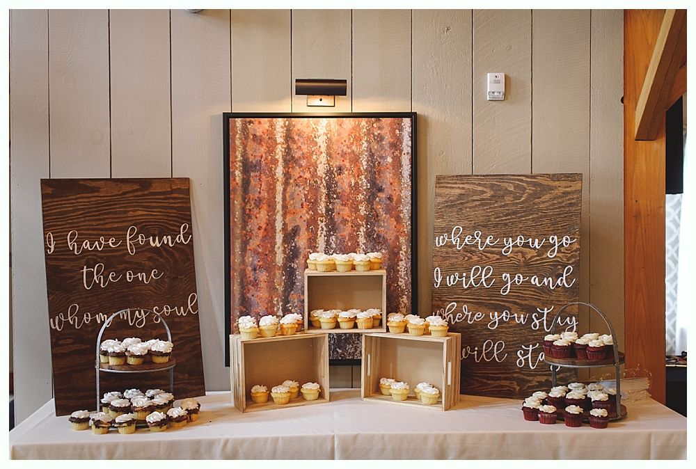 Cupcake display with wooden signs, crates, and tiered stands on a white table.