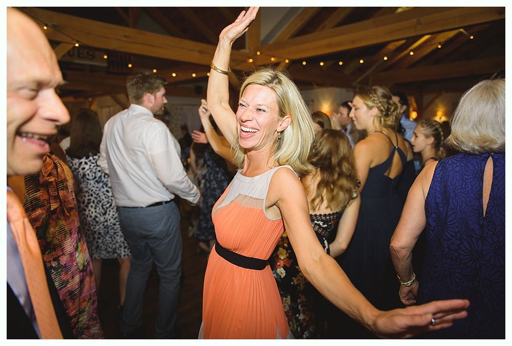 Woman dancing with arm raised at a party, wearing an orange dress. Other people in the background.