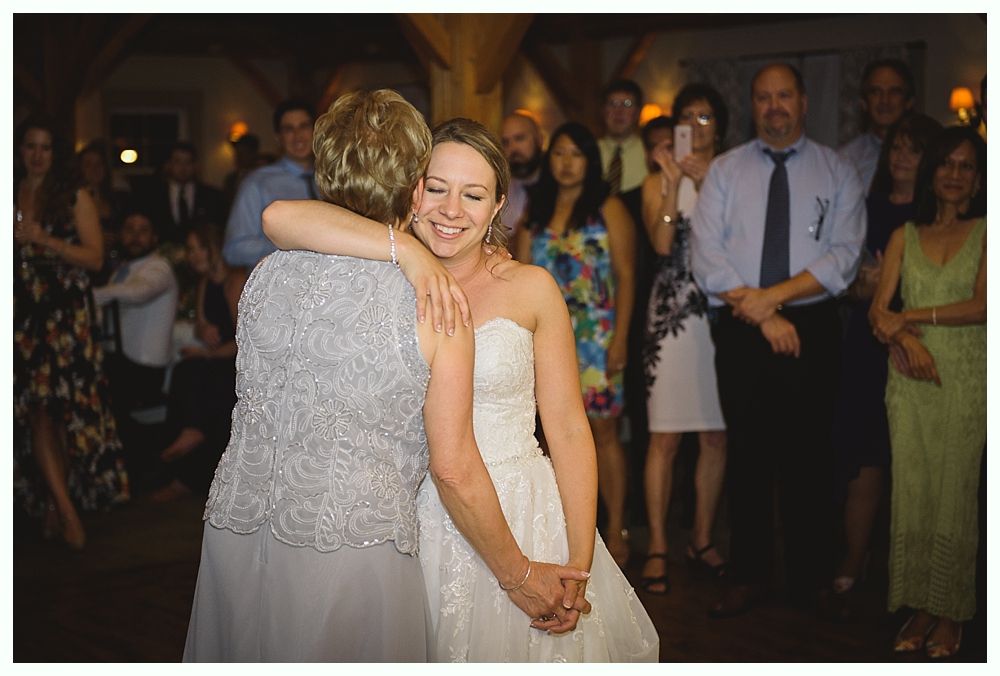 Bride embracing woman on dance floor at reception, surrounded by guests.