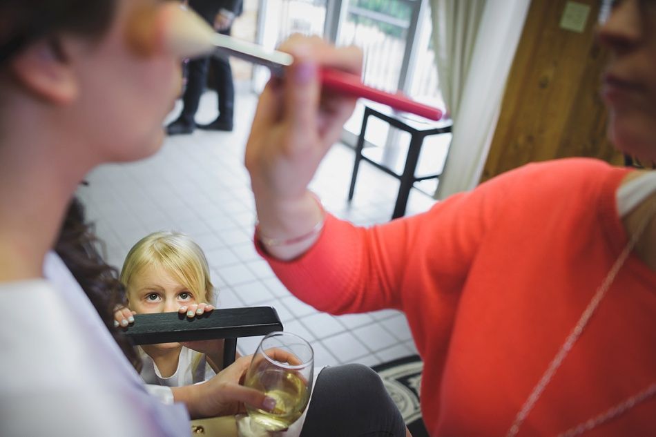 Woman applying makeup; child peers from behind a chair.