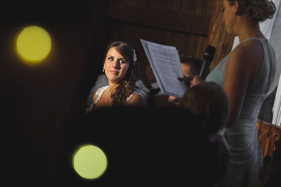 Bride smiles during a wedding ceremony as a woman reads from a paper. Soft lighting.
