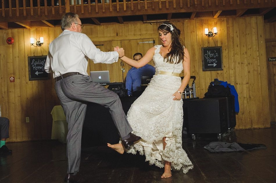 Bride and man dancing with bare feet in a wooden room; both are kicking feet up in the air.