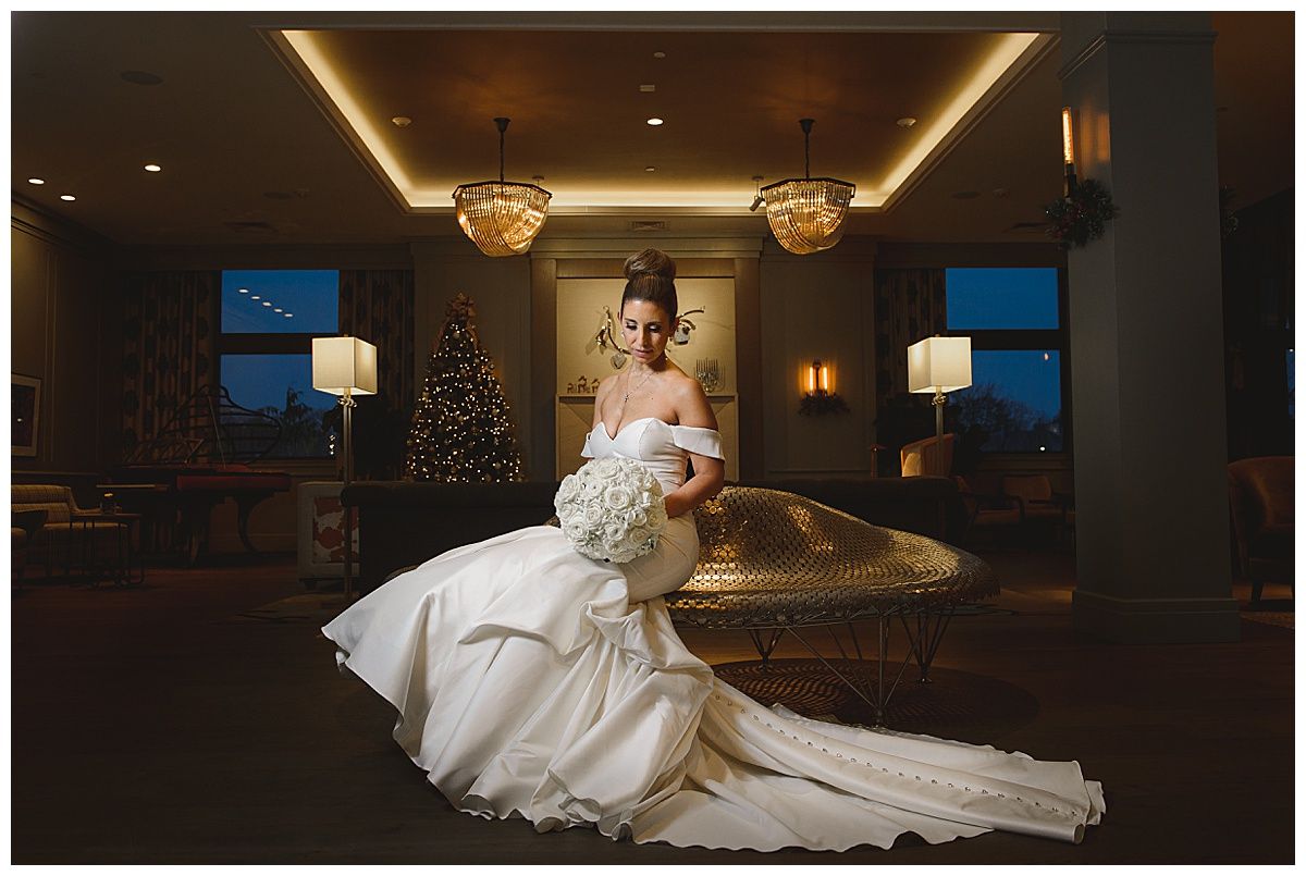 Bride in a white gown holding a bouquet, standing in a decorated room with a Christmas tree and chandeliers.