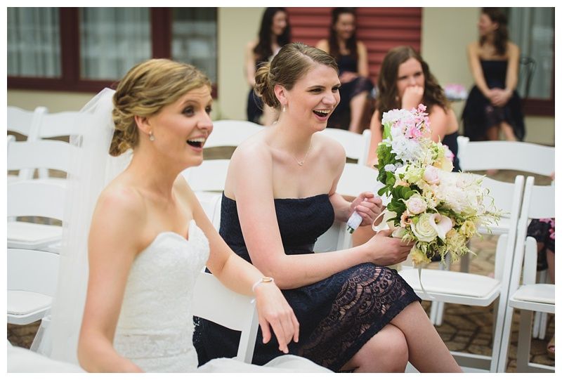 Bride with arms up, making a funny face, groom looking at his hand, cake cutting in background.