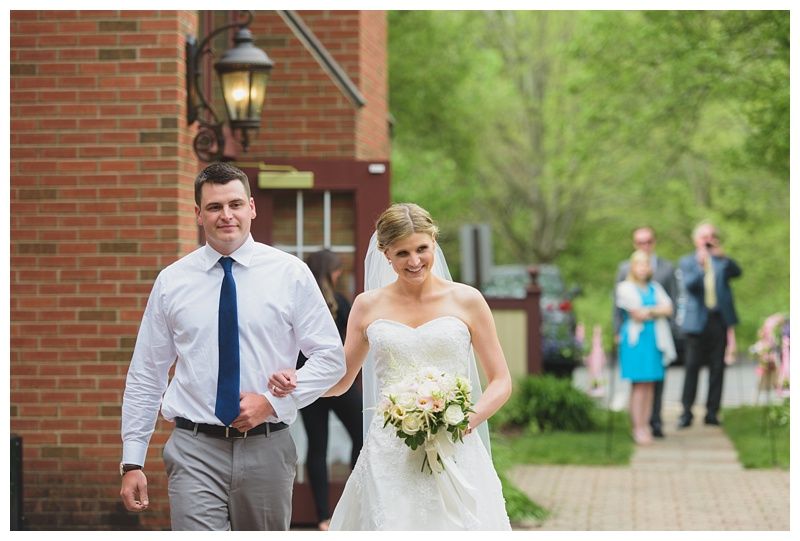 Bride with arms up, making a funny face, groom looking at his hand, cake cutting in background.