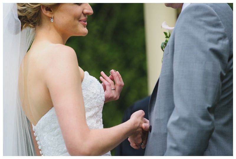 Bride with arms up, making a funny face, groom looking at his hand, cake cutting in background.