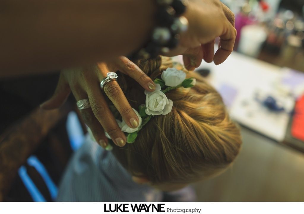 Hands adding white flower hair accessory to a bun, with rings on the fingers.