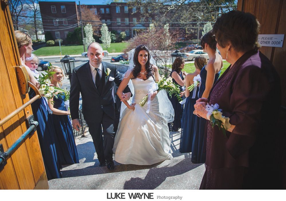 Bride and groom exiting a church after their wedding, smiling, surrounded by the wedding party.