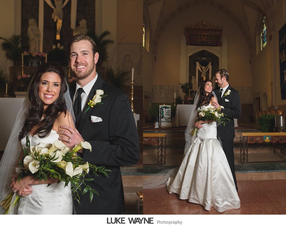Bride and groom posing inside a church. The bride wears a white dress and holds a bouquet. The groom wears a black suit.