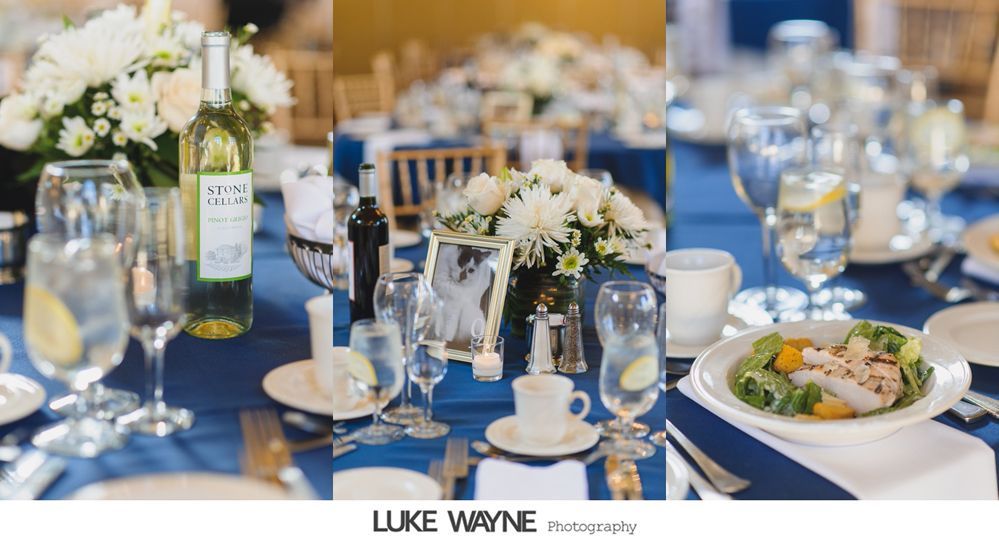 Wedding reception table setting with blue tablecloth, floral centerpiece, and glassware.
