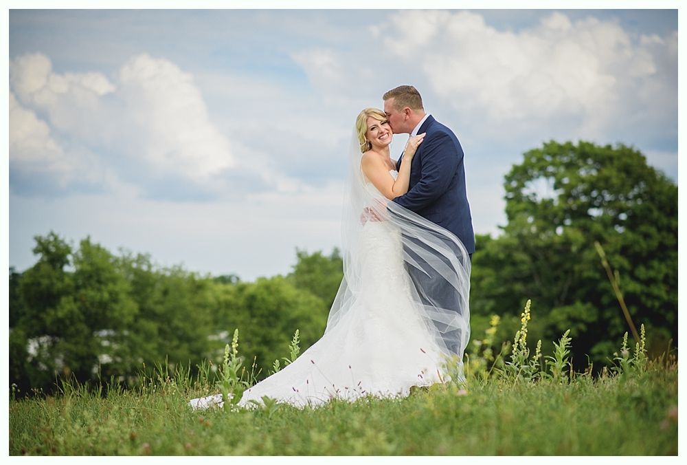 Bride with arms up, making a funny face, groom looking at his hand, cake cutting in background.