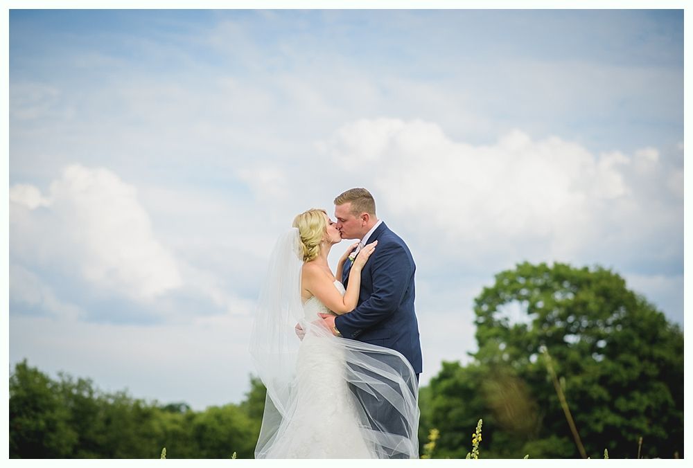 Bride with arms up, making a funny face, groom looking at his hand, cake cutting in background.