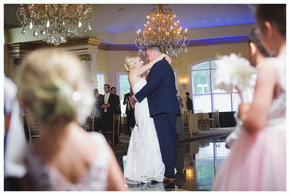 Bride with arms up, making a funny face, groom looking at his hand, cake cutting in background.