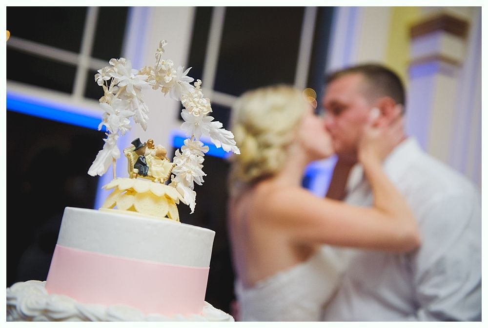 Bride with arms up, making a funny face, groom looking at his hand, cake cutting in background.
