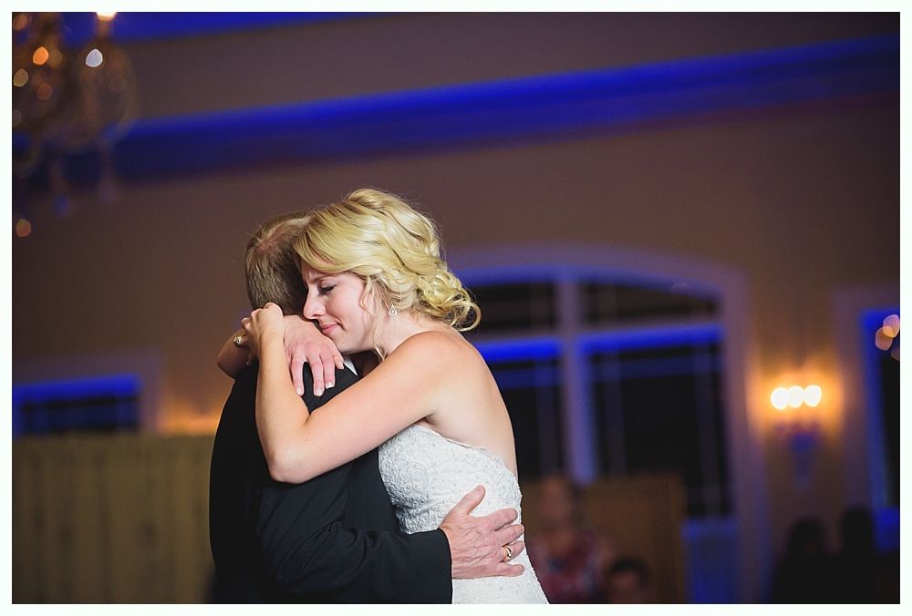 Bride with arms up, making a funny face, groom looking at his hand, cake cutting in background.
