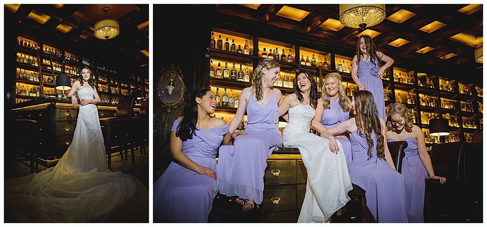 Bride and bridesmaids pose in a dimly lit bar. The bride in white sits with her bridesmaids in lavender dresses.