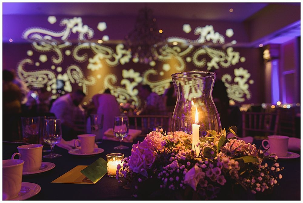Formal dining table with candle centerpiece and illuminated paisley design on the wall.