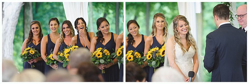 Bridesmaids and bride at a wedding ceremony; dark dresses, sunflower bouquets, outdoors. Bride and groom face each other.
