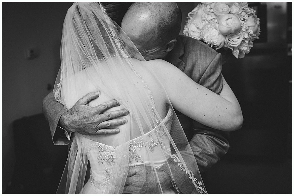 Bride in wedding dress embracing person in suit, with bouquet.