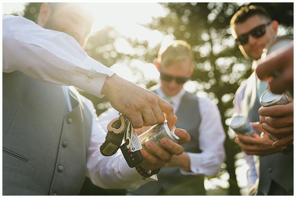 Men in gray vests opening small cans outdoors, sunlight in the background.