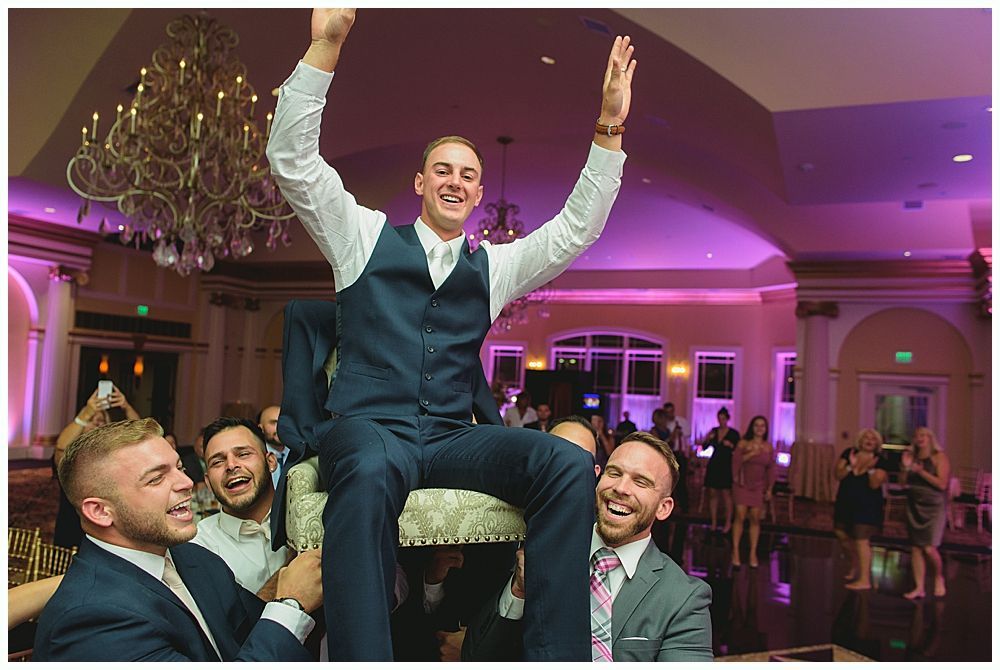 Man raised on a chair by two others, celebrating in a ballroom.
