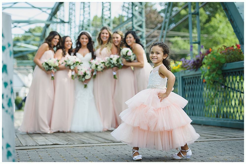 Flower girl poses on a bridge with bridesmaids in pink dresses; wedding scene.