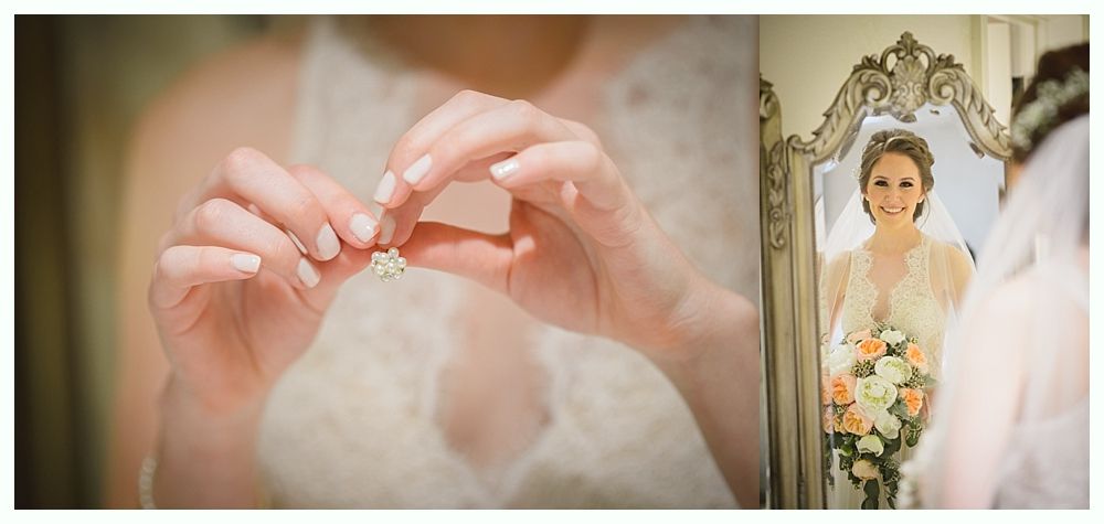 Bride holding an earring, looking at her reflection in a decorative mirror.
