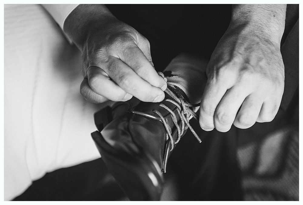 Hands tying shoelaces on a shiny black dress shoe. Black and white photo.