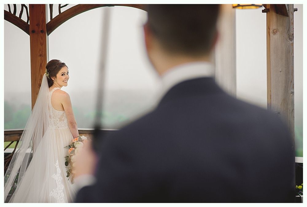 Bride in white gown smiles at groom; outdoor ceremony setting.