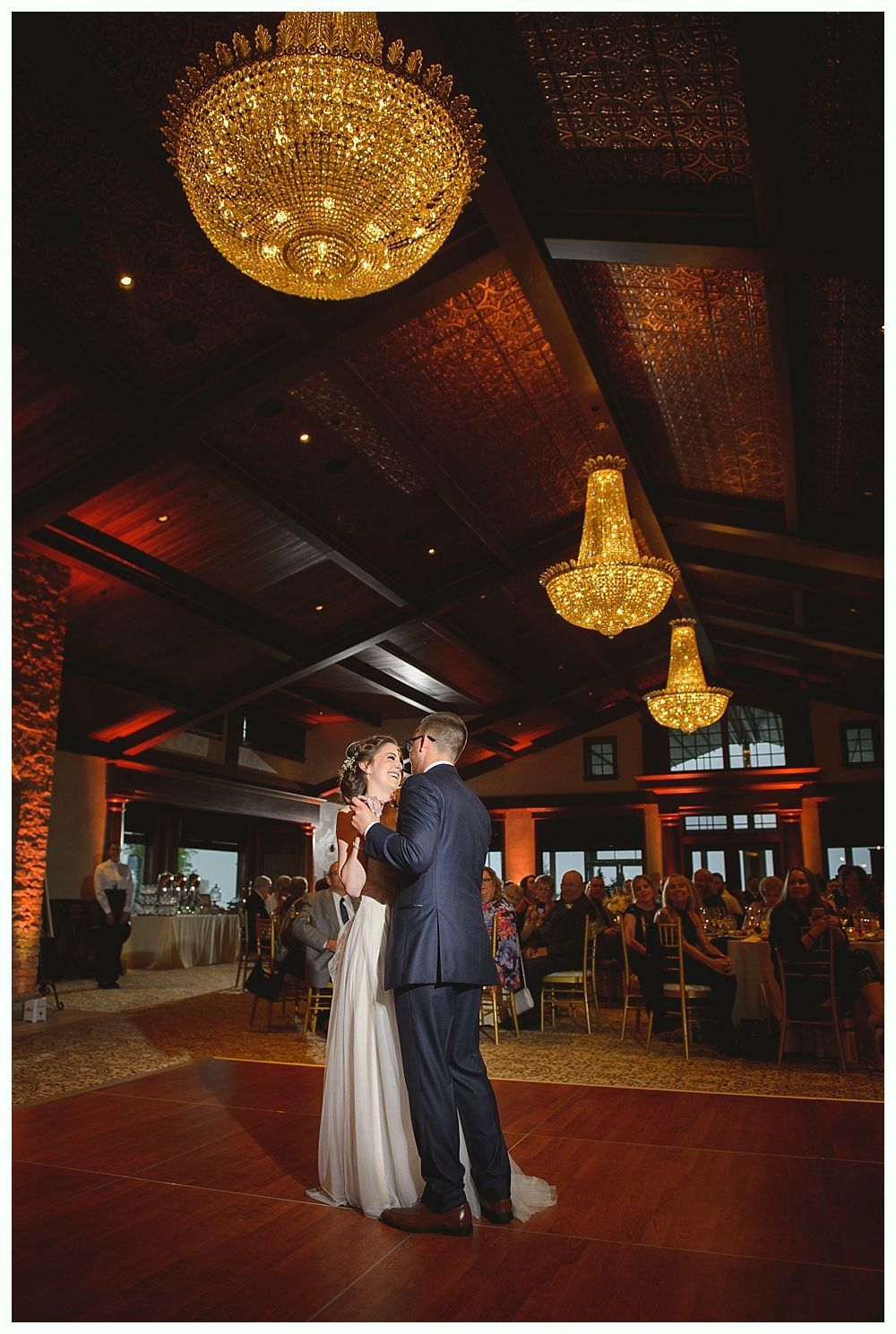 Couple dancing at wedding reception under golden chandeliers.