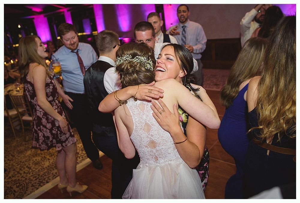 Bride hugged by woman on dance floor at wedding reception.
