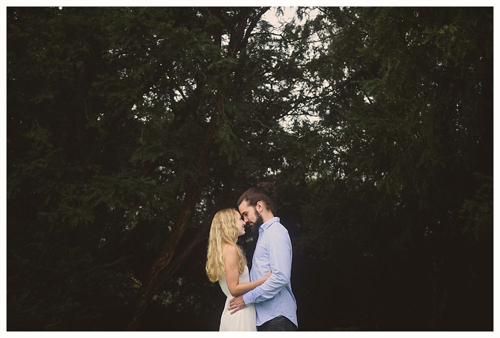 Couple embraces under a large tree. The woman has long blonde hair, the man has a beard.