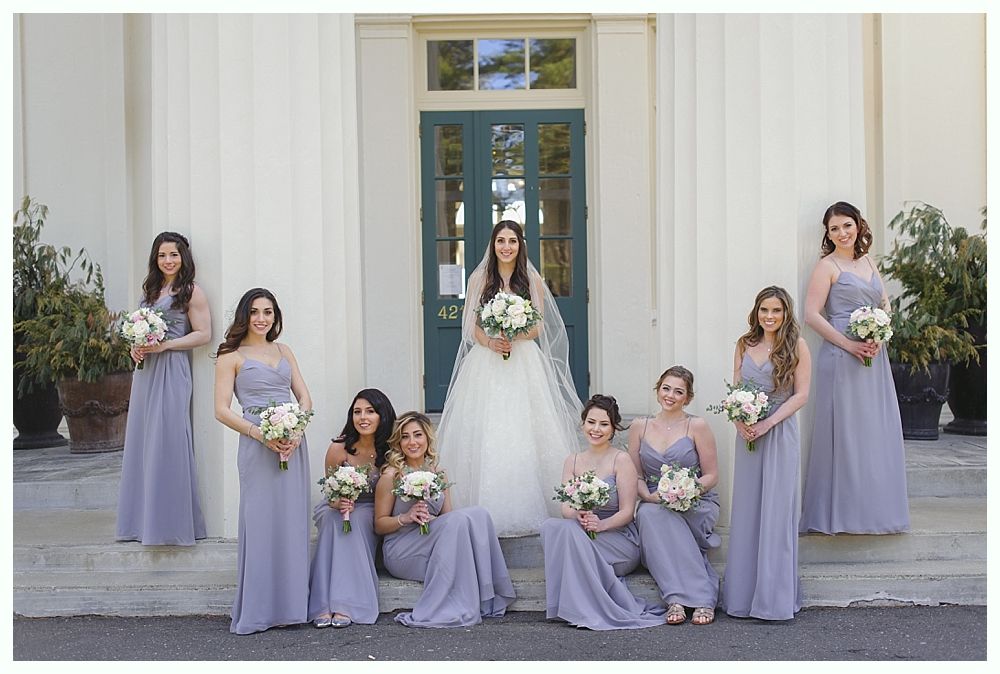 Bride and bridesmaids in lavender gowns posing on steps in front of a building with a green door and columns.