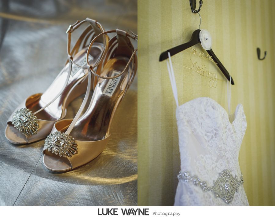 Wedding shoes and dress; high heels with crystal embellishments and a lace strapless gown with a jeweled belt, hanging on a wall.