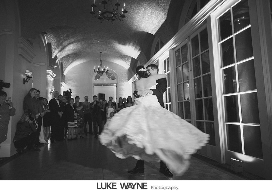 Bride and groom dance at reception; voluminous dress swirls. Guests watch near windows.