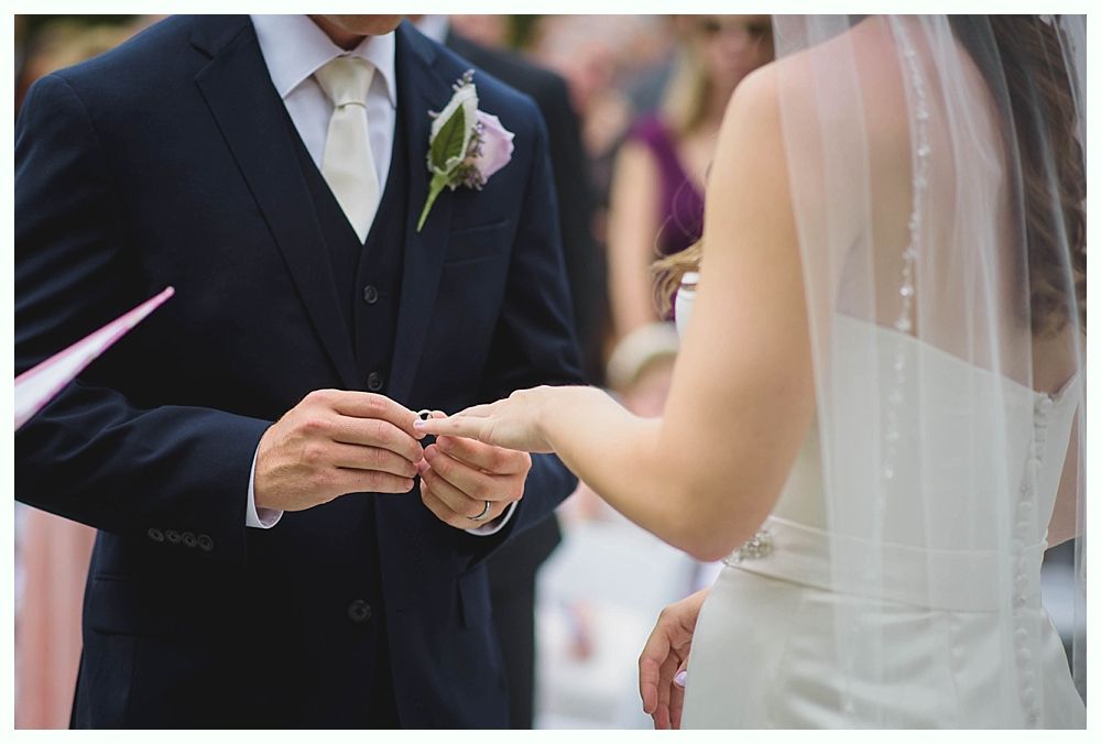 Bride with arms up, making a funny face, groom looking at his hand, cake cutting in background.
