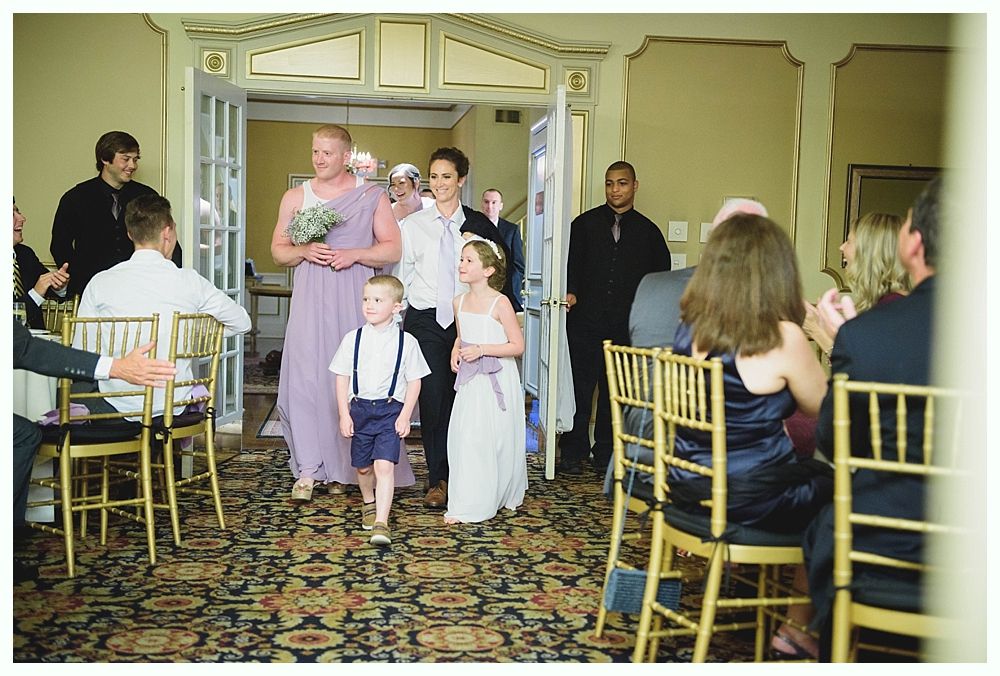 Bride with arms up, making a funny face, groom looking at his hand, cake cutting in background.