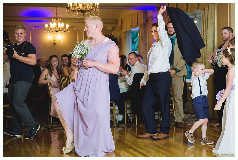 Bride with arms up, making a funny face, groom looking at his hand, cake cutting in background.
