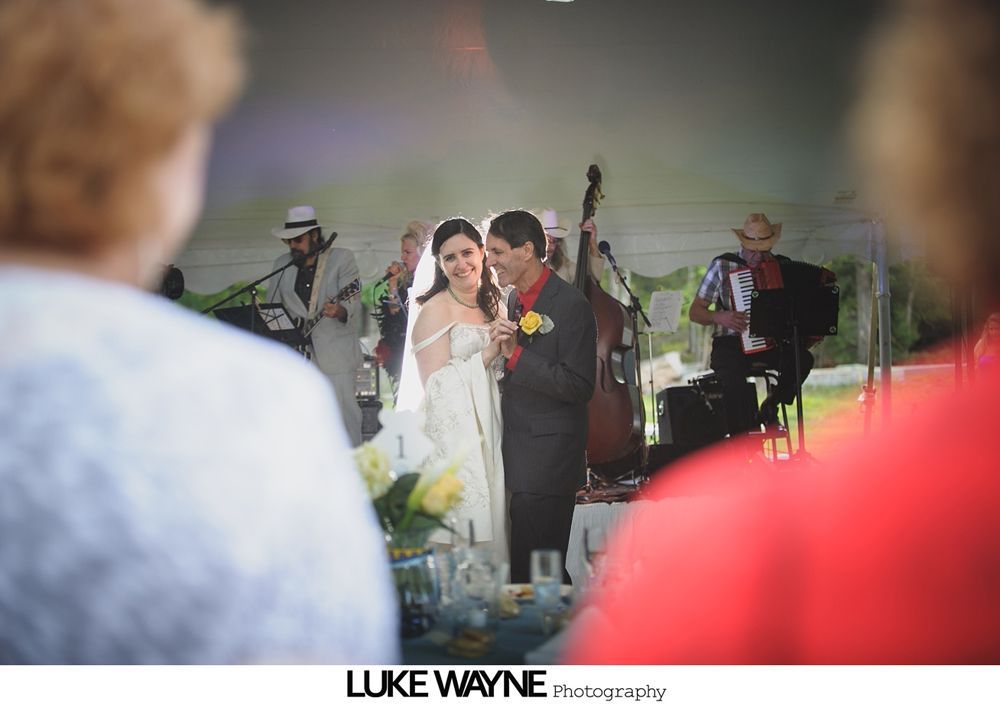 Group photo at a wedding reception. Bride and groom centered, surrounded by guests in formal attire.