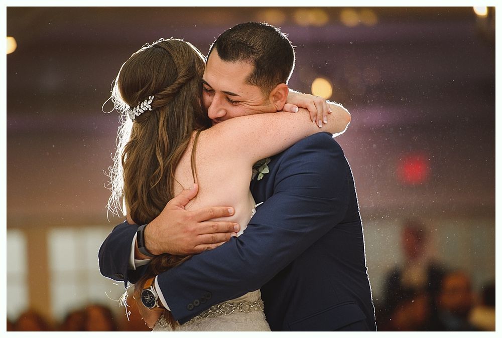 Bride and groom dance at a wedding reception in a rustic barn, surrounded by guests.